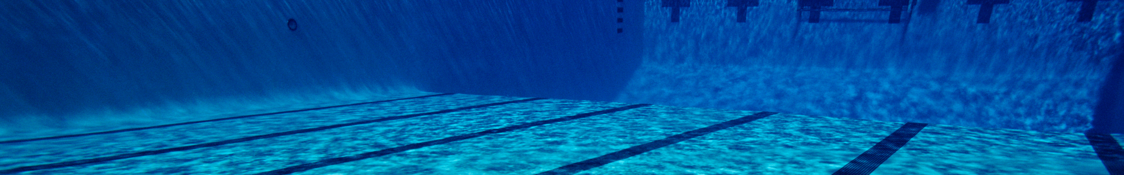 Underwater view of a clear blue swimming pool with lane markings and tiled walls, shot from below the surface